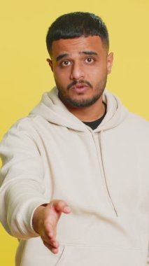 Kameraya uzanan dost canlısı Hintli genç adam, el sıkışma teklif ediyor, nazik bir gülümseme, davetiye, dayanışma ve güven göstergesi olarak karşılıyor. Sarı arka planda izole edilmiş Arap adam.