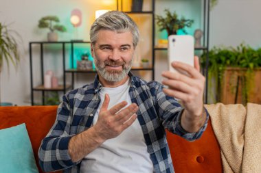 Son sınıf öğrencisi internetteki internet uygulaması ve sosyal ağda dalga mutlu sohbet ve iletişim ile video görüşmesi yapıyor. Beyaz sakallı, orta yaşlı adam akıllı telefon kullanıyor. Oturma odasındaki kanepede oturuyor.