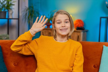 Beyaz çocuk evde mutlu bir şekilde selamlaşırken gülümseyerek el sallıyor. Kanepeye oturur, kameraya bakar, neşeyle merhaba der hoş geldin der ya da elveda der, neşe ve dostluk sergiler.