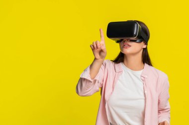 VR kulaklık takan genç bir kadın ellerini havaya kaldırıyor ve sanal dünyaya hayran kalıyor. Sarı arka planda izole edilmiş bir kız dijital deneyime olan hayranlığını ve heyecanını ifade ediyor.