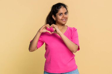 Hintli kadın parmaklarını nazikçe kalbe yerleştiriyor, kameraya doğru gülümsüyor, derin bir sevgi gösteriyor. Arap kızı samimi duygular ifade ediyor. Şefkat, sevgi, arkadaşlık ve olumlu duygular..