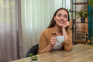 Genç bir kadın sıcak kahve fincanı tutarak evinde oturuyor ve hayatı huzurlu ve mutlu hissederek düşünüyor. Kafkasyalı kız yavaşça nefes alıyor hafif aromanın tadını çıkarıyor ve sakin bir neşe ve minnettarlık anına kucak açıyor.