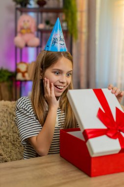 Masada oturan genç kız doğum gününü kutluyor ve sürpriz mutluluğu ifade eden bir hediye açıyor. Okul çocuğu heyecanla aldığı hediyeye sevinçle tepki veriyor.