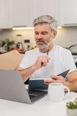 Evde çalışan orta yaşlı bir adam kulaklıklarla ders çalışıyor ve notlar yazıyor. Olgun adam kanepeye oturur, dinler, duraksar, ödevler için ödev ekler, gözden geçirir ve liste yapar.