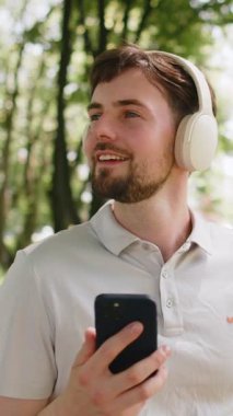 Sporcu spor koşucusu adam yürüyor ve akıllı telefon kullanıyor kablosuz kulaklıkla müzik dinliyor. Şehir parkında egzersiz kardiyosu. Genç koşucu sağlıklı yaşam tarzını seviyor..
