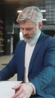 Beyaz tenli orta yaşlı işadamı belgelerle çalışıyor, bilgileri analiz ediyor, gazete okuyor mali rapor hazırlıyor. Takım elbiseli mutlu girişimci ofis lobisindeki grafik belgelerini inceliyor..