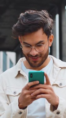 Genç Hintli adam cep telefonuyla kutlama yapıyor. İyi haber kazan, piyango zaferi kazan, açık havada internetten bağış yap. Şehir merkezindeki Hintli mutlu adam. İş adamları yaşam tarzları