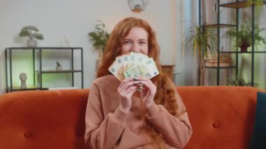 Başarılı, zengin, beyaz bir kadın elinde avro banknotlarıyla evdeki kanepede oturuyor. Mutlu yetişkin kız çevrimiçi piyango oyunu kazanıyor tatil planlama bütçe hesaplama konsepti.