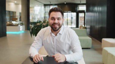 Şok olmuş genç iş adamının kameraya bakışları şaşırmış yüz ifadesini gösteriyor. Mutlu sakallı adam modern ofis lobisinde beklenmedik bir haber terfisi ile seviniyor..