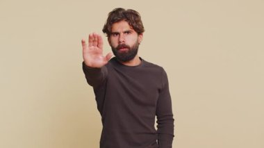 Hintli bir adam, el hareketini durdurma, bitirme uyarısı, erişimi yasaklama, iletişimi kesme, vücut dili, tehlike. Bej arka planda Latin Hintli genç bir adam. İnsan yaşam tarzları.