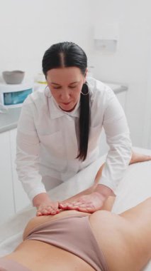 Güzellik doktoru, genç bayana spa antiselülit bacaklar, kalçalar ve kalça masajı yaptırıyor. Zayıflatma, vücut şekillendirme. Fizyoterapist kozmetoloji seansı. Dikey