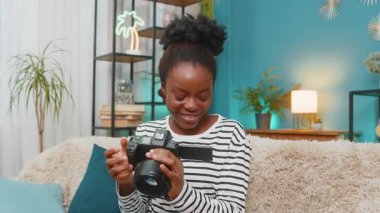 Afro-Amerikalı genç bir kadın evdeki rahat oturma odasında kanepede oturuyor gülümsüyor ve kameradaki başarılı fotoğrafları eleştiriyor. Çalışmaktan gurur duyuyorum. Çekimleri zevk ve zevkle analiz ediyorum.