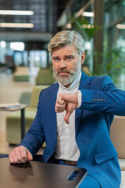 Hoşlanmamak. Takım elbiseli üzgün işadamı ofis lobisinde oturmuş işaret dilini gösteriyor hoşnutsuzluğunu, memnuniyetsizliğini ve kötü işini dile getiriyor. Otel odasında ciddi bir olgun adam var..