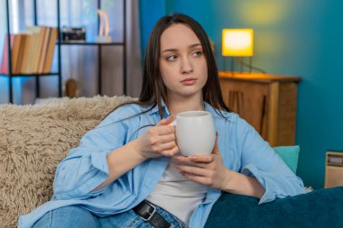 Evdeki üzgün genç kadın sessizce kanepede oturuyor, sessizce çay içiyor, derin düşünceler ve yalnızlık içinde. Kafkasyalı kız melankolik, duygusal yansıma, yalnızlık ve içsel üzüntü yaşıyor..