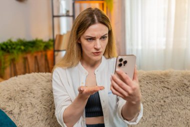 Orta yaşlı bir kadın evdeki akıllı telefondan yorum yapıyor, somurtuyor ve hayal kırıklığı stresiyle elini sallıyor. Genç yetişkin bir kız, olumsuz geri bildirime karşı sinirsel tepki gösterir. Görünürde sinirli ve gergin..