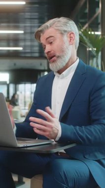 Modern ofis lobisinde dizüstü bilgisayarda çalışan orta yaşlı bir işadamı çalışanlarıyla online iletişim videosu görüşmesi yapıyor, patron. Bilgisayarın webcam görüntülerine bakan yönetici destek servisleri.