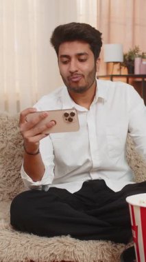 Evde patlamış mısır yiyen Hintli bir adam, akıllı telefondan film izleyip, keyfine bakıyor. Arap adam rahatlamış, ekrana odaklanmış, eğlenceye dalmış, eğlenceli bir heyecan yaşıyor.