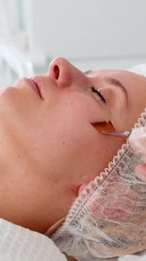 Kozmetik uzmanı özel asit serumu uyguluyor. Tıbbi kremi nemlendiriyor. Güzel beyaz bir kadının yüzü soyuluyor. Güzellik salonunda yaşlanmayı önleyen estetik tedavi prosedürü