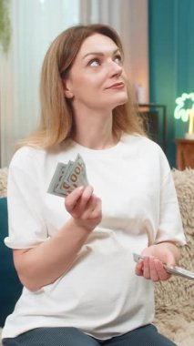 Evde oturan orta yaşlı hamile bir kadın nakit para sayıyor. Doğum planlama bütçesi, mali güvence için para tutuyor. Kanepedeki kız kendini çok güvende hissediyor. Tasarruf hesapları bebek için hazırlanıyor..