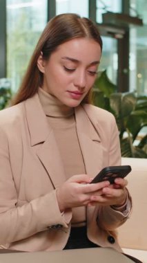 Kafkasyalı genç iş kadını cep telefonu mesajlaşması kullanıyor akıllı telefon sosyal medya uygulamaları üzerinde çalışarak içeriği paylaşıyor, modern ofis lobisinde dinleniyor. Otel odasında oturan bayan.