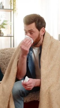 Evdeki hasta genç adam kanepeye oturur, battaniyeye sarınır, hapşırır ve çabucak mendile uzanır. Kafkasyalı adam burnunu siliyor, iyi görünmüyor, muhtemelen soğuk algınlığı ya da grip belirtileri gösteriyor.