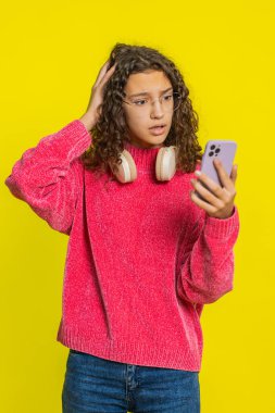 Üzgün Kafkasyalı kız akıllı telefon daktilo kullanıyor, oyun oynuyor, aniden piyango sonucuna şaşırıyor kötü şans kaybı şanssız haber. Sarı arka planda izole edilmiş mutsuz ergen çocuk.