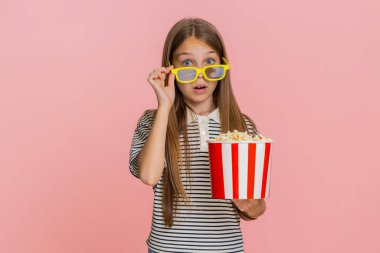 Genç kız mutlu bir şekilde patlamış mısır yiyor, televizyonda eğlenceli bir çizgi film izliyor, neşeli bir şekilde gülüyor, geniş bir kesime gülümsüyor, eğlenceli animasyon sahnelerinden haz alıyor. Pembe arka plandaki okul çocuğu.