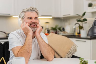 Evde orta yaşlı bir adam kablosuz kulaklıkla müzik dinliyor. Ellerine yaslanıyor, gülümsüyor ve hayaller kuruyor. Masadaki olgun adam sorumluluk almayı düşünüyor. Gelecek planı sakin ve kendinden emin..