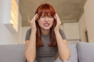 Evdeki genç kadın başını şiddetli bir baş ağrısı ile tutuyor gözlerini kapatıyor şakaklara sürtünüyor kısa bir ara veriyor. Kanepedeki kızıl saçlı kız yavaş nefes alıyor. Stres ve ekran geriliminden kurtulmaya ihtiyacı var. Sakinleşip dinlenmek istiyor.