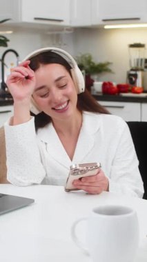 Evde kablosuz kulaklık takan genç bir kadın akıllı telefondan mesaj yolluyor. Kanepede oturan beyaz kız dizüstü bilgisayarını kontrol eder sosyal uygulama cevapları sohbet etmek için mutlu ruh halini rahatlatır.