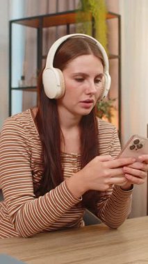 Evde genç bir kadın kulaklıkla verimlilik podcast 'i dinliyor ve akıllı telefondan fikirler yazıyor. Masadaki beyaz kız not tutuyor iş için planlar yapıyor ve öğrenim sırasında sakin kalıyor