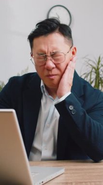 Diş sorunları. Ofiste çalışan Asyalı işadamı yanaklarına dokunuyor, korkunç bir ifade ile gözlerini kapatıyor diş ağrısı, hassas dişler, çürükler. Resmi takım elbiseli Çinli bir erkek.