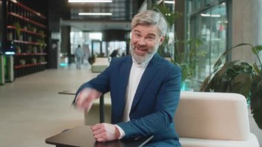 Seni seçiyorum. Kafkasyalı orta yaşlı işadamı kamerayı işaret ederek, mutlu bir ifadeyle bakarak, işe alma seçimini yapıyor. Resmi takım elbiseli mutlu adam modern ofis otel lobisinde oturuyor..