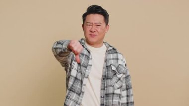 Hoşlanmamak. Mutsuz Asyalı adam, hoşnutsuzluğunu, memnuniyetsizliğini ve olumsuz tepkilerini belirterek işaret gösteriyor. Yakışıklı Çinli olgun bir adam bej arka planda kapalı yerde izole edilmiş.