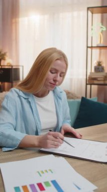 Genç bir kadın evdeki sözleşme belgelerini inceliyor, sayfaya bakıyor ve önemli noktaları dikkatle inceliyor. Beyaz kız masada oturuyor, yeni anlaşma imzalıyor, müşteriyle iyi bir anlaşma yapıyor.