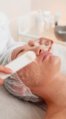 Kozmetik uzmanı, beyaz bir kadının özel nemlendirici kremini sürüyor, yüzünü ovuyor, soyuyordu. Güzellik salonunda yüz bakımı yaşlanmayı önleyen kozmetik masaj prosedürü. Güzellik tedavisi. Dikey