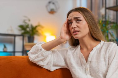 Hasta kadın baş ağrısı problemini tedavi etmek için tapınakları ovuyor, tansiyon, migren, stres, evde acı içinde kıvranıyor yüksek tansiyon. Beyaz kız kanepede, kapalı bir odada. Yaşam Tarzları