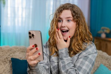 Evde cep telefonunu kaydıran genç bir kadın, haber, indirim ya da Kafkasyalı bayanı temsil eden kazanan sonuç için heyecanlanıyor. Kanepedeki kızıl saçlı kız haykırıyor. Şaşırmış, sevinçli bir kutlama reaksiyonu gösteriyor.