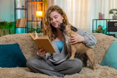 Genç, rahat, Kafkasyalı, kızıl saçlı kadın evde koltukta köpeğe kitap okuyor. Yumuşak bir sesi ve sıcak bir gülümsemesi var. Evcil hayvan sessizce onun yanında uzanıyor, sakince dinliyor ve günün sonunda nazik bağlantılarını paylaşıyor..