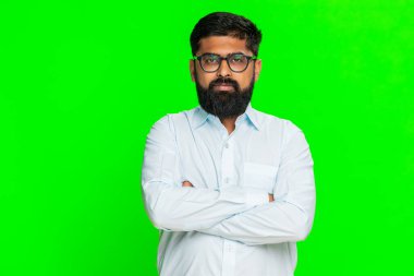 Hintli bir adam kollarını kavuşturur ve ciddi bir yüz ifadesiyle otoriter bir tavır takınır. Yeşil krom anahtar arka planda izole edilmiş Arap adam sertlik ve kontrol ifade ediyor