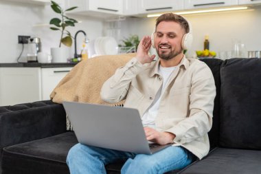 Evde genç bir adam, sakin müzik çalarken ve sabit bir tempoyla odaklanırken dizüstü bilgisayarla çalışıyor. Kafkasyalı kanepede rahat bir şekilde oturan adam ritmi ve odaklanmayı sürdürüyor ve işini neşeyle bitiriyor..
