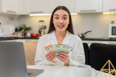 Evdeki genç kadın nakit para sayıyor. Avro, maaş ve yatırım planlarından gurur duyuyor. Kanepede oturan beyaz kız fatura yığınında oturuyor. Bütçe takibi, finans, meblağı ve hedefleri hesaplıyor.