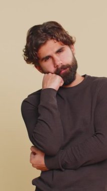 Sıkılmış, umursamaz Hintli adam ifadesi, sıkıcı hikayelerden bıkmış, iletişim konuşmalarıyla ilgilenmeyen, hoşnutsuz, ilgisiz. Bej renkli stüdyo arka planında izole edilmiş genç sakallı adam..