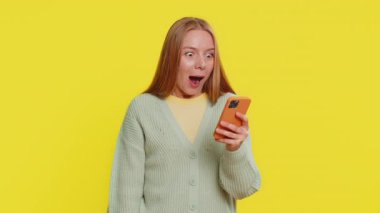 Şanslı orta yaşlı kadın akıllı telefondan sevinç çığlıkları atıyor, para dolu banknotlar alıyor zaferi kutlayan online piyango kumarhanesi oyunu oynuyor. Sarı arka planda izole edilmiş mutlu kız