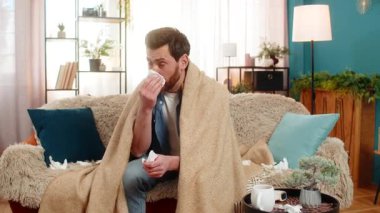 Evdeki hasta genç adam kanepeye oturur, battaniyeye sarınır, hapşırır ve çabucak mendile uzanır. Kafkasyalı adam burnunu siliyor, iyi görünmüyor, muhtemelen soğuk algınlığı ya da grip belirtileri gösteriyor.