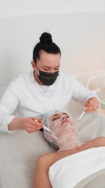 Enzim terapisi. Güzellik uzmanı, genç yetişkin bir kadının yüzüne nemlendirici kimyasal krem maske takıyor. Kaplıcadaki kız cilt bakımı. Yüz kozmetolojisi tedavisi. Dikey