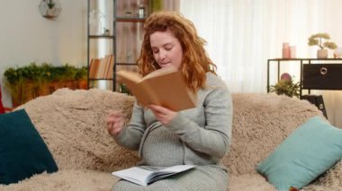 Hamile genç kadın evde ebeveynlik kitabından notlar yazıyor, ciddi bir ifadeyle konsantre oluyor, gelecekteki anneliğe hazırlanıyor. Kız düşünceli bir şekilde fikirleri kaydediyor, öğrenme ve özeni kucaklıyor..