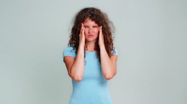 Başını kapalı tutan genç bir kadın baş ağrısı, stres, acı verici gerilim ve tükenmiş bir ifade yaşıyor. Gri arka plandaki kız rahatsız edici migren belirtileri gösteriyor..