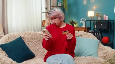 Genç bir kadın mutlu bir şekilde online alışveriş yapıyor, akıllı telefon ve kredi kartı kullanıyor, gülümsüyor, başını sallıyor. Beyaz kız e-ticaretten zevk alıyor, neşeli olumlu alıcı jesti, koltukta oturuyor.