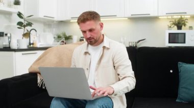 Evdeki genç adam dizüstü bilgisayarı açar çalışma sistemini başlatır ve odaklanmış ve kendinden emin bir gülümsemeyle hızlı yazar. Kanepede oturan beyaz adam görevleri kontrol ediyor. Notlar yazıyor. Verimli bir ruh hali ve açık bir hedef..